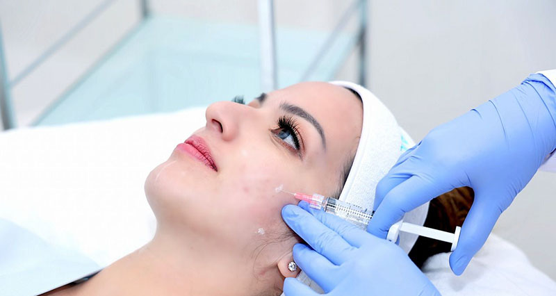 دختری که کلاه به سر دارد و پزشک به صورت او پروفایلو تزریق می کند